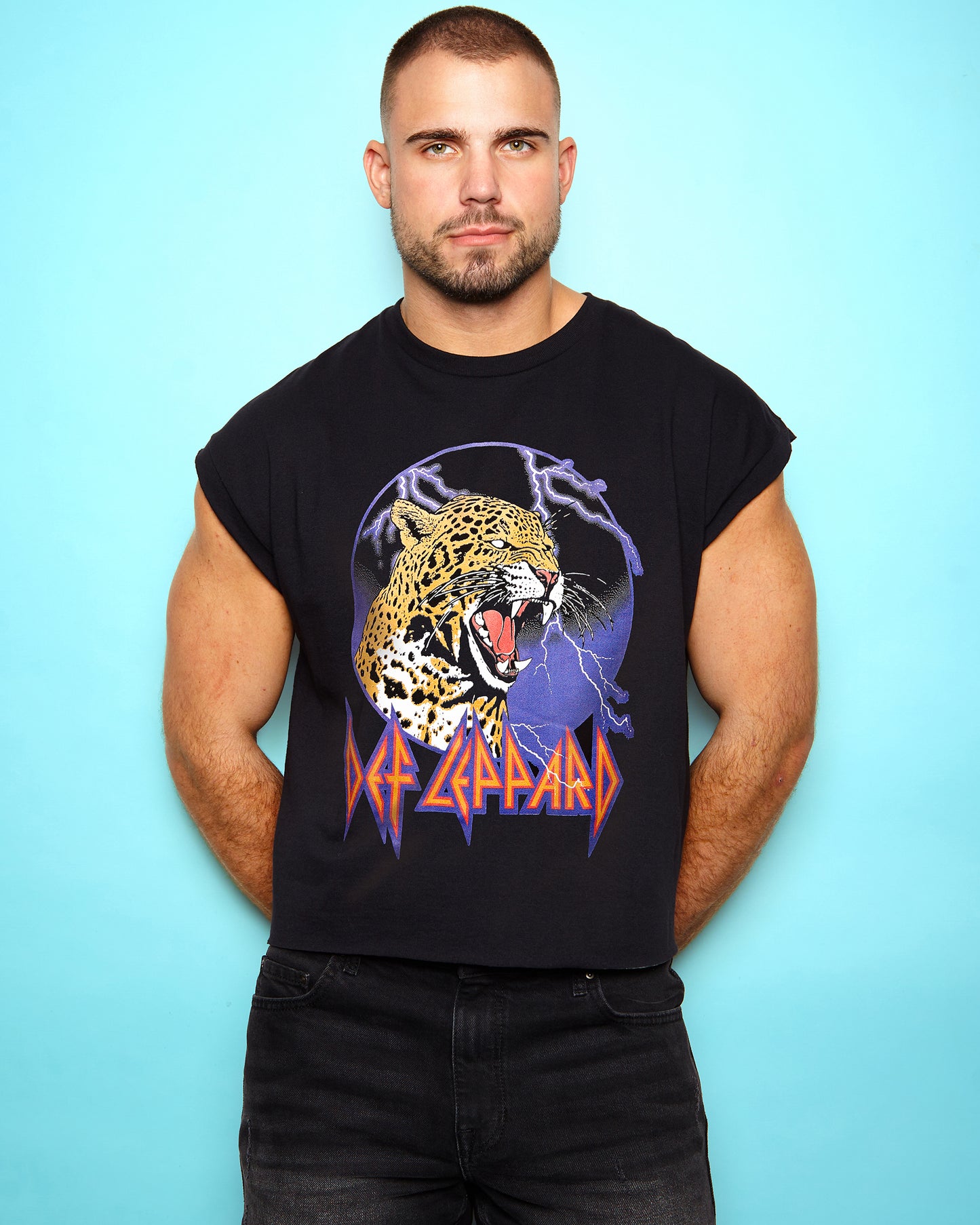 Man wearing a black sleeveless shirt with a Def Leppard logo on a light blue background